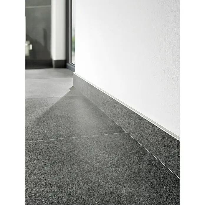 Art-Tec by Palazzo Feinsteinzeugfliese - 60 x 120 cm, Onyx, Matt - Detailaufnahme von grauen Bodenfliesen mit passenden Sockelleisten, die einen sauberen Übergang zur weißen Wand bilden.