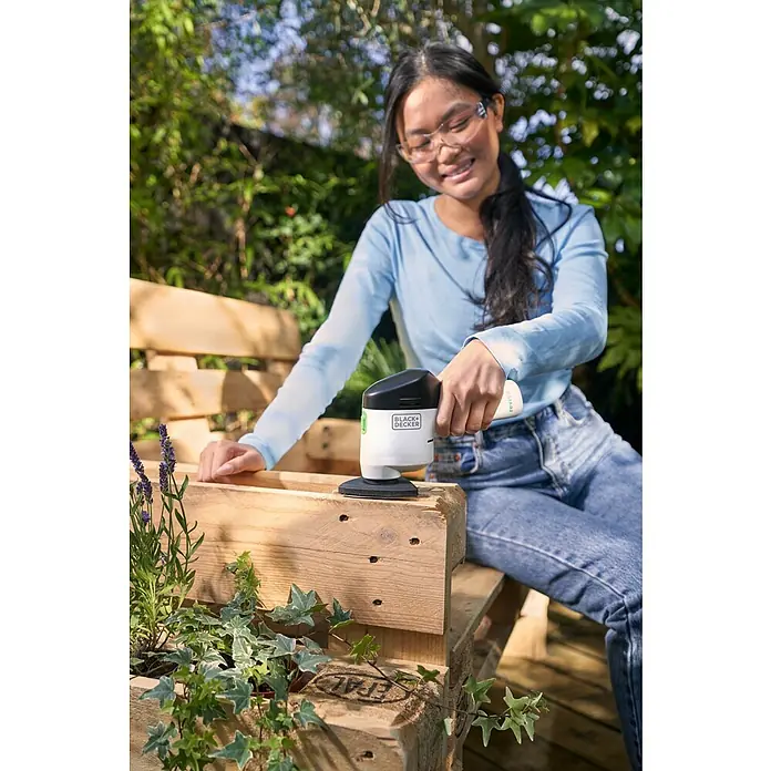 Black+Decker reviva Lijadora delta de batería - 12 V, 1,5 Ah, 11.000 r.p.m. - Mujer usando una lijadora de mano Black+Decker para trabajar en una caja de madera en el jardín.