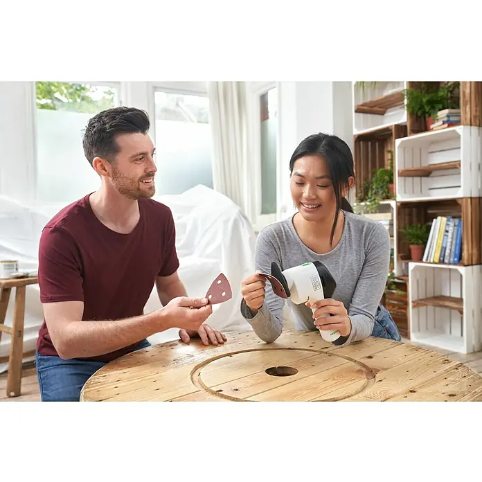 Black+Decker reviva Lijadora delta de batería - 12 V, 1,5 Ah, 11.000 r.p.m. - Una mujer sujeta papel de lija a una multi-lijadora inalámbrica Black+Decker REVIVE mientras un hombre está a su lado mirando.