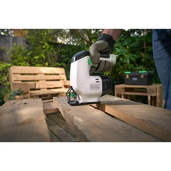 Black+Decker reviva Sierra de calar de batería - 12 V, 1 batería, 1,5 Ah - Primer plano de una sierra de calar Black+Decker sostenida por una mano enguantada, cortando una tabla de madera.
