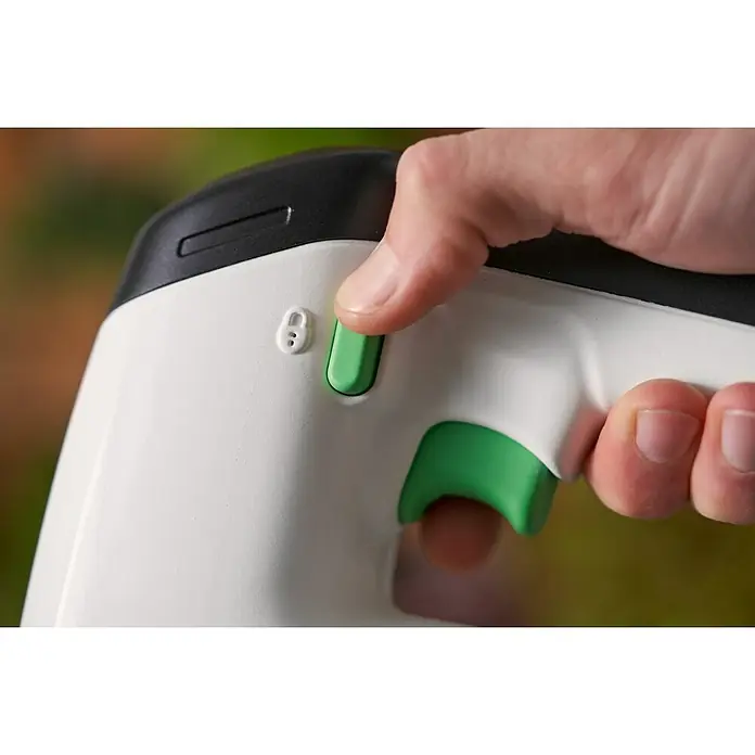 Black+Decker reviva Sierra de calar de batería - 12 V, 1 batería, 1,5 Ah - Primer plano de una mano que presiona el botón verde de un dispositivo blanco de diseño ergonómico. Característica de seguridad y gatillo visibles.