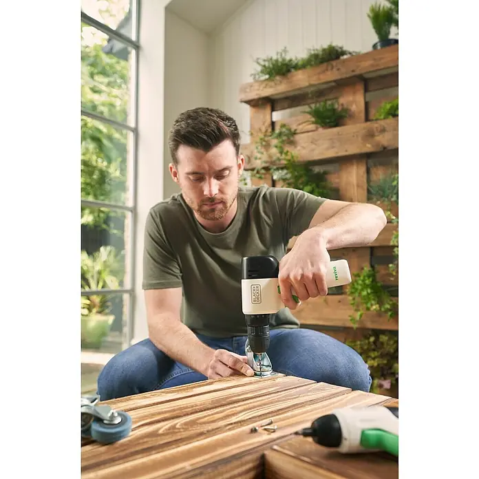 Black+Decker reviva Taladro atornillador de batería - 12 V, 1 batería, 1,5 Ah, 26 Nm - Un hombre sujeta una ruedecilla a una tabla de madera con un taladro inalámbrico Black+Decker REVIVA. El taladro es inalámbrico y tiene un diseño moderno.
