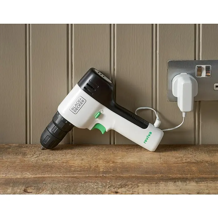 Black+Decker reviva Taladro atornillador de batería - 12 V, 1 batería, 1,5 Ah, 26 Nm - Taladro inalámbrico Black+Decker Reviva en blanco y negro con detalles verdes enchufado a una toma de corriente para cargar.