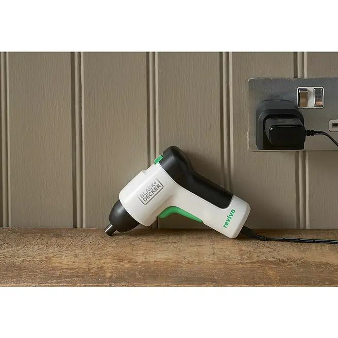 Black+Decker reviva Atornillador de batería - 3,6 V, 1 batería, 1,5 Ah, 5,5 Nm - Primer plano de un destornillador inalámbrico Black+Decker Reviva que descansa sobre una superficie de madera junto a una toma de corriente con un cargador enchufado.