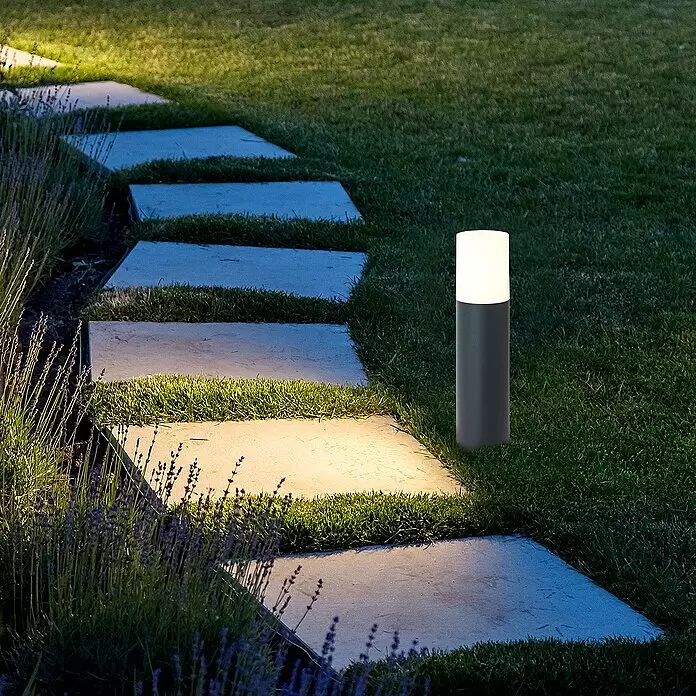 Brilliant Außensockelleuchte - 28 W, Farbe Gehäuse: Anthrazit, Ohne Leuchtmittel - Zylindrische Außenleuchte in Dunkelgrau und Weiß beleuchtet nachts einen Gartenweg aus Trittsteinen.