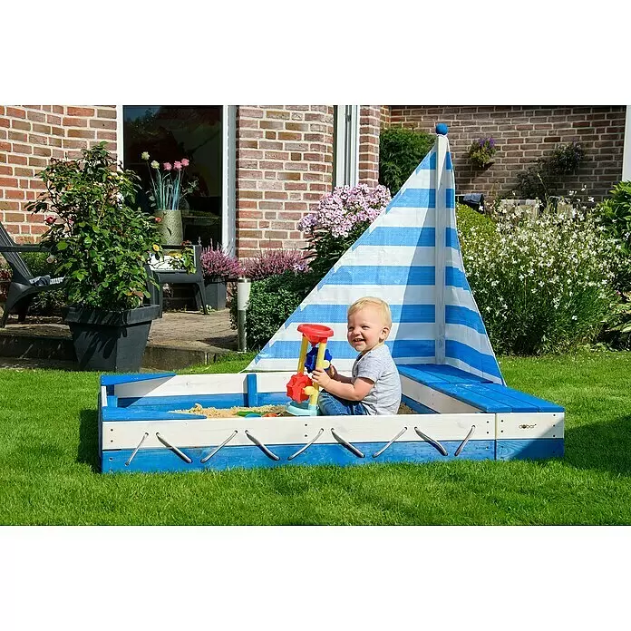 Dobar Sandkasten Maritim - 140 x 120 x 117 cm, Holz, Blau/Weiß - Ein glückliches Kind spielt in einem blau-weißen bootförmigen Holzsandkasten mit gestreiftem Segel.