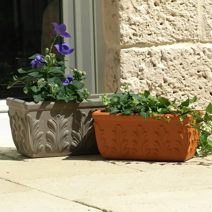 Balkonkasten - Max. Außenlänge: 30 cm, Terracotta - Nahaufnahme von zwei dekorativen Pflanzgefäßen mit Reliefmuster, eins in Taupe mit Glockenblumen und eins in Orange mit Efeu, auf einem sonnigen Steinboden.