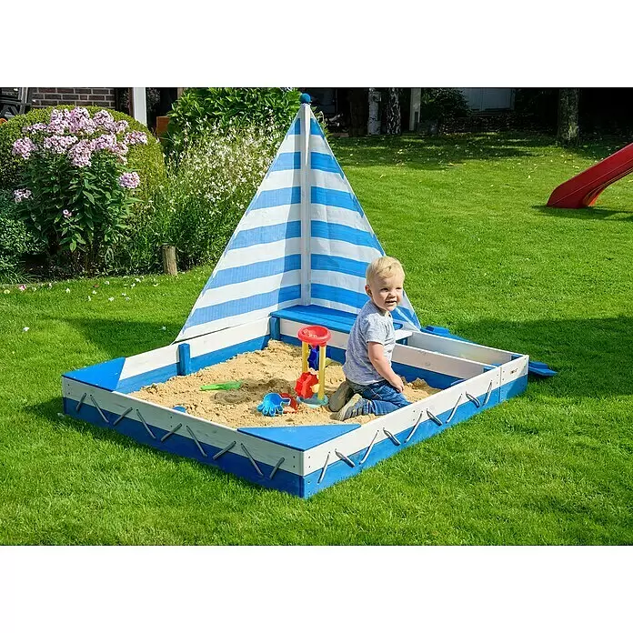 Dobar Sandkasten Maritim - 140 x 120 x 117 cm, Holz, Blau/Weiß - Blau-weißer Holzsandkasten mit gestreiftem Segel, ein Kind spielt im Sand mit bunten Spielsachen.