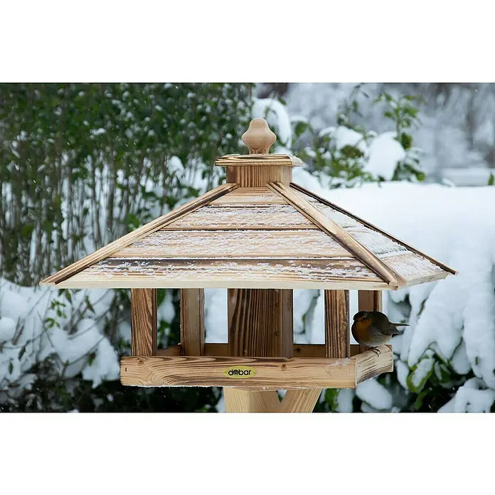 Dobar Vogelfutterhaus Lumbre - L x B x H: 50 x 50 x 36 cm, Braun, Holz - Ein hölzernes Vogelhaus mit Schnee auf dem Dach, auf dem ein Rotkehlchen sitzt, mit dem "dōbar"-Logo an der Seite.