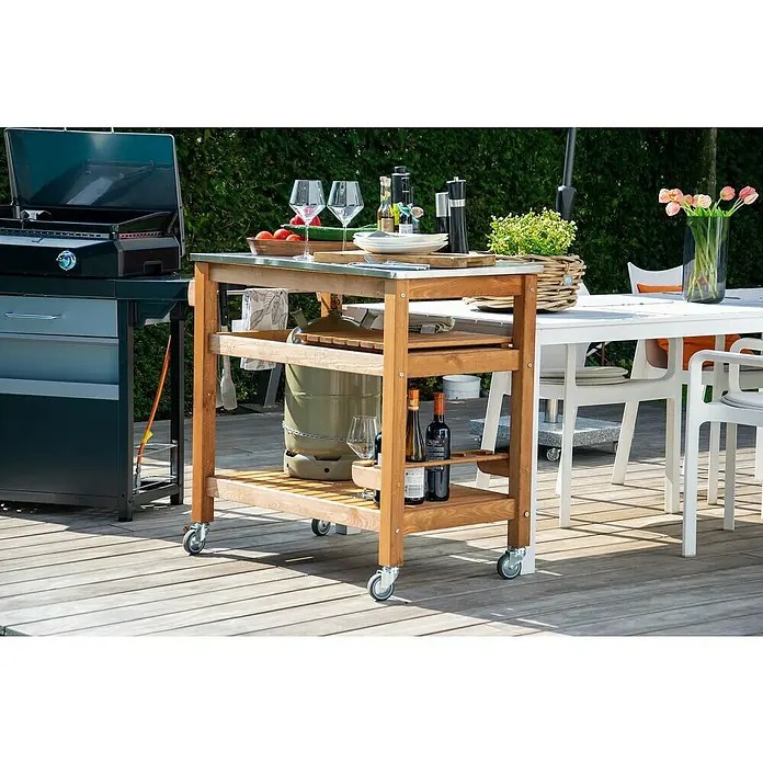Dobar Beistellwagen - L x B x H: 94 x 58 x 90 cm, Braun - Ein Outdoor-Küchenwagen aus Holz mit Rädern steht auf einer Terrasse, beladen mit Geschirr, Getränken und einer Gasflasche.