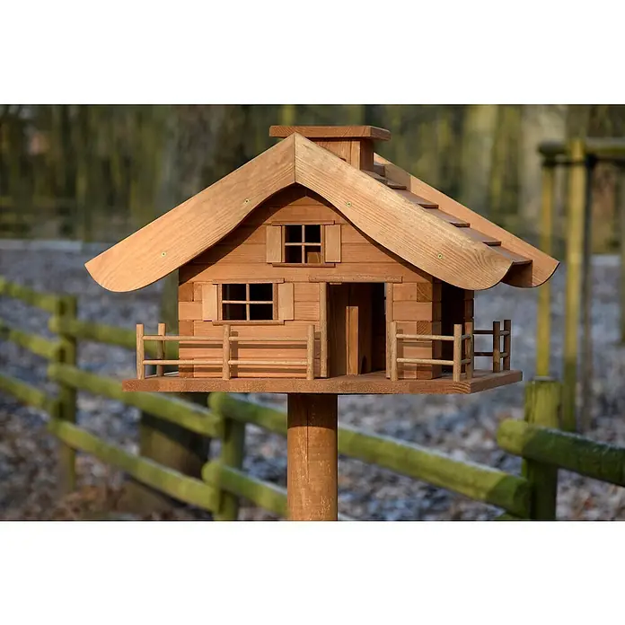 Dobar Vogelfutterhaus Almhütte - L x B x H: 66 x 66 x 136,5 cm, Braun, Holz - Detailaufnahme eines hölzernen Vogelhauses im Blockhausstil mit Satteldach und kleinem Zaun auf einem Holzpfosten im Garten.