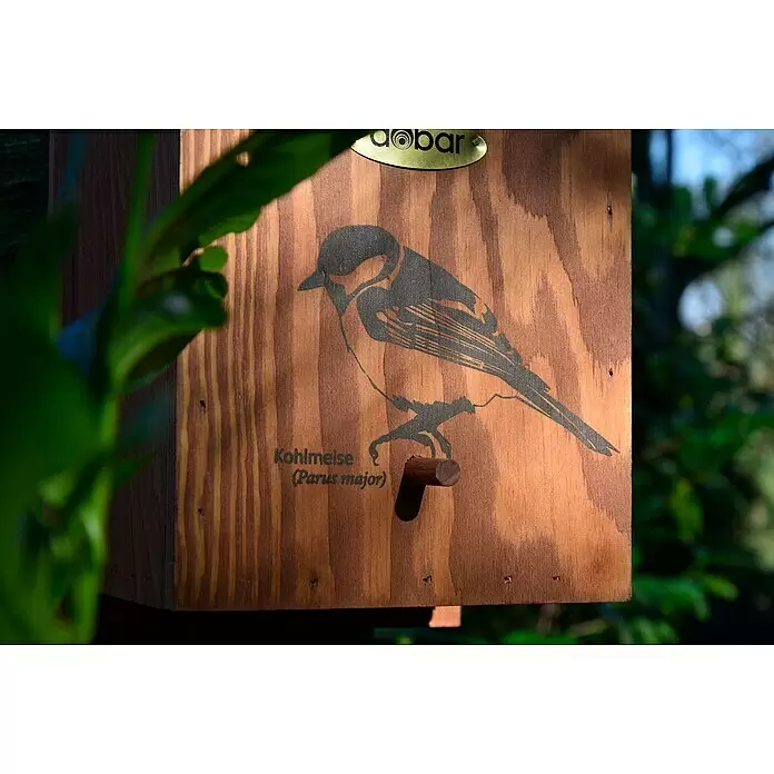 Dobar Nistkasten - L x B x H: 17 x 18 x 35 cm, Braun, Holz - Hellbrauner Nistkasten aus Holz mit schwarzer Vogelsilhouette und Text, ausgestattet mit einer Holzstange, draußen teils hinter grünen Blättern.