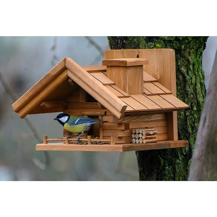 Dobar Vogelfutterhaus St. Moritz - L x B x H: 33 x 24,5 x 21 cm, Braun, Holz - Ein Meisenknödelhalter im Holzhaus-Design, auf einem Baum befestigt, mit einer Blaumeise, die darauf landet. Perfekt für Vogelliebhaber.