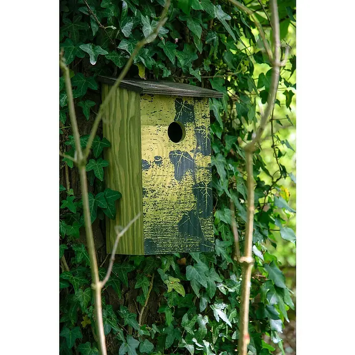Dobar Nistkasten Fagus sylvatica - 15,5 x 14,5 x 30 cm, Braun, Holz - Ein gelbes Vogelhaus mit Blattmuster ist an einem Baum befestigt, umgeben von dichtem Grün. Bietet einen sicheren Nistplatz für Vögel.
