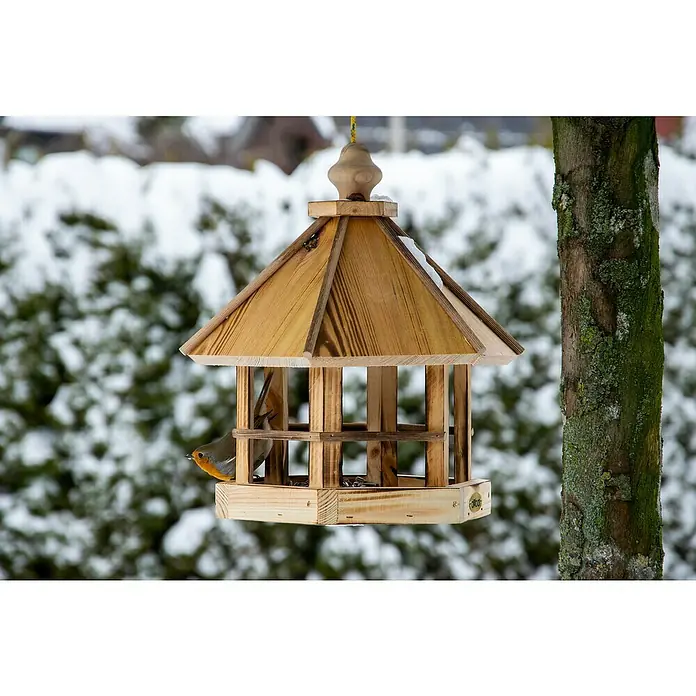 Dobar Vogelfutterhaus Caliente - L x B x H: 29 x 29 x 34 cm, Braun, Holz - Nahaufnahme eines hölzernen Vogelhauses im Winter mit einem kleinen Vogel, der darin sitzt und pickt.