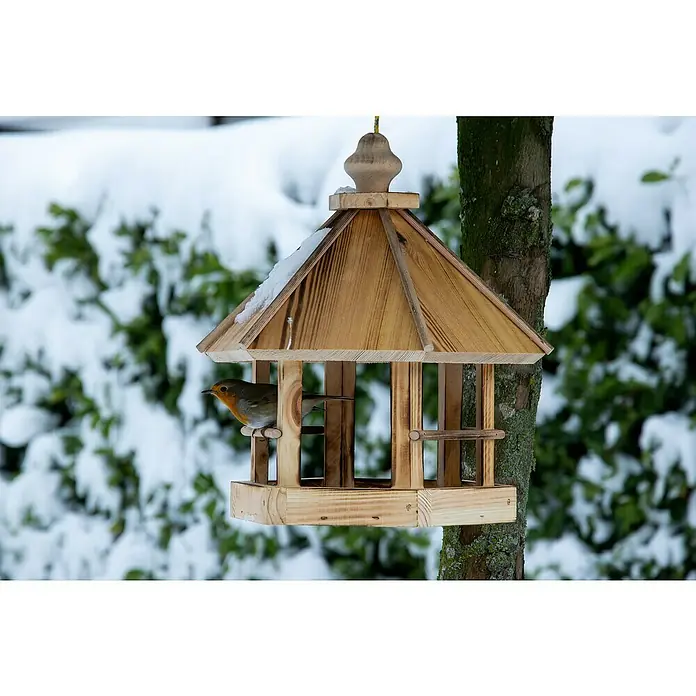 Dobar Vogelfutterhaus Caliente - L x B x H: 29 x 29 x 34 cm, Braun, Holz - Ein hölzernes Vogelhaus mit Schnee auf dem Dach und einem Rotkehlchen darin, das an einem Baum befestigt ist, vor einem verschneiten Hintergrund.