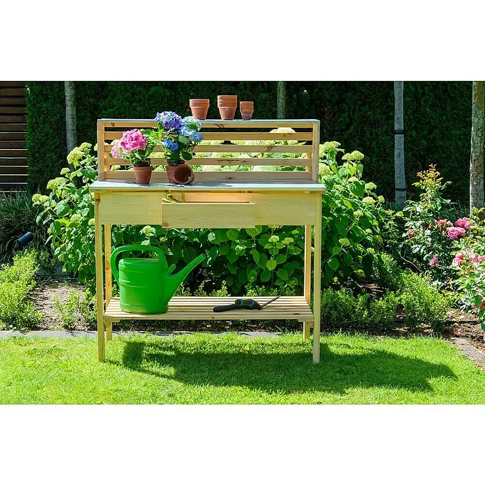 Dobar Pflanztisch Buche - L x B x H: 117 x 62 x 124 cm - Gartentisch aus Holz mit Schublade, Ablage und Blumen, eine grüne Gießkanne steht auf der Ablage.