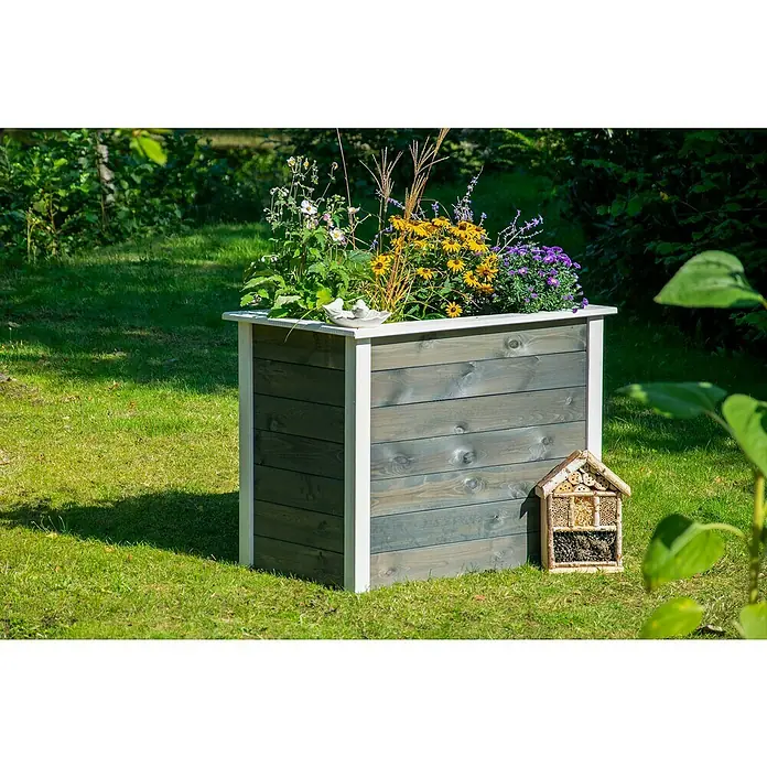 Dobar Hochbeet Two-Tone - L x B x H: 108 x 65 x 80 cm, Holz, Anthrazit/Weiß - Ein grauer Blumenkasten aus Holz mit weißen Akzenten, gefüllt mit bunten Blumen, steht auf einer grünen Wiese. Daneben ein Insektenhotel.