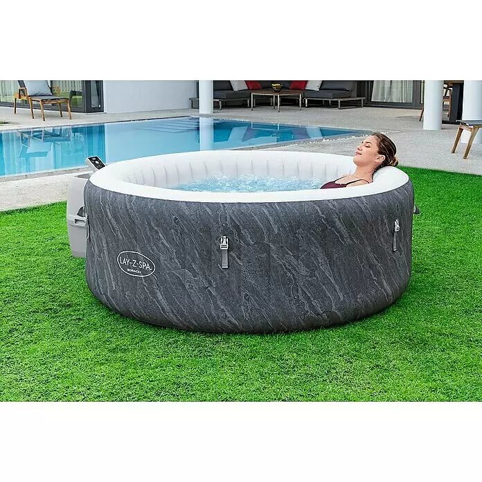 Bestway Lay-Z-Spa Mobil-Whirlpool Boracay Air Jet - Ø x H: 180 x 66 cm, Schwarz, 669 l - Dunkelgrauer, marmorierter aufblasbarer Whirlpool mit einer Frau, die darin neben einem Pool entspannt.