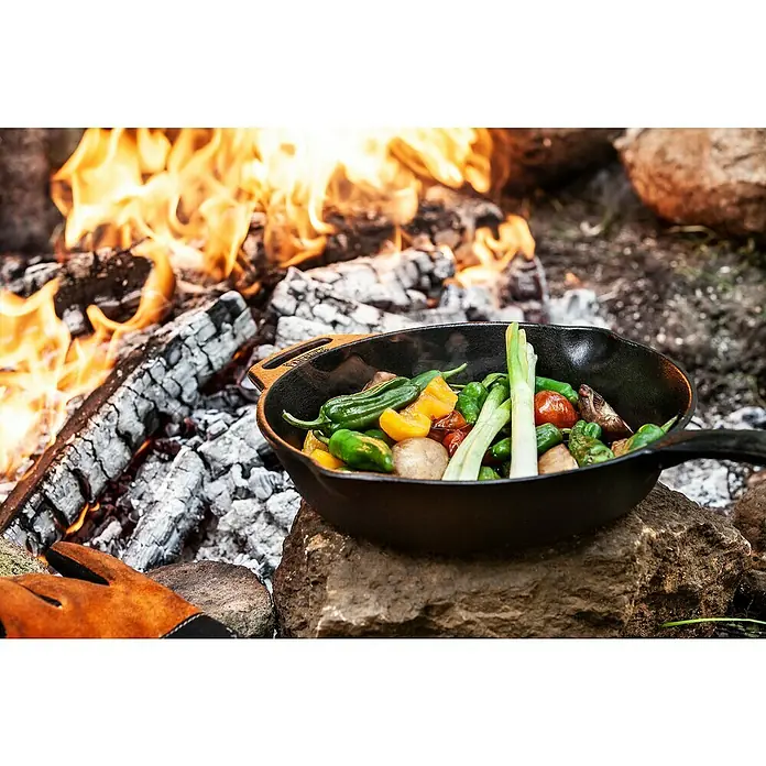 Petromax Grillpfanne - Ø x H: 30 x 4,5 cm, Gusseisen - Ein Teller mit frischem Gemüse wird über einem Lagerfeuer zubereitet, wodurch ein köstliches Gericht entsteht.