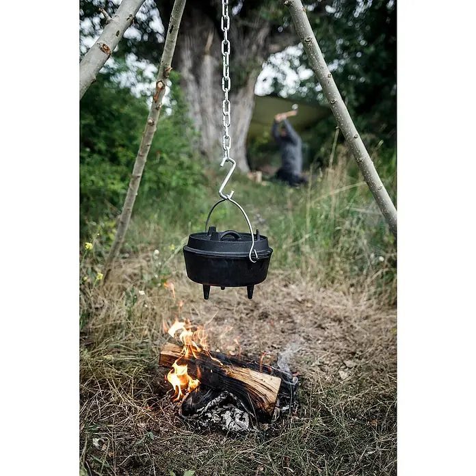 Petromax Dutch Oven - Ø x H: 25,2 x 16 cm, Gusseisen, 1,6 l, Mit Füßen - Ein Dutch Oven hängt an einer Kette über einem offenen Feuer, ideal zum Kochen im Freien.