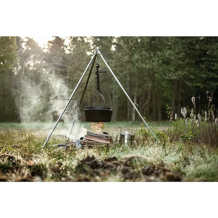Petromax Dutch Oven - Ø x H: 42 x 20 cm, Gusseisen, 10,8 l, Planer Boden - Ein Dutch Oven hängt an einem Dreibein über einem Lagerfeuer, daneben steht ein Kessel. Outdoor-Kochgeschirr in der Natur.