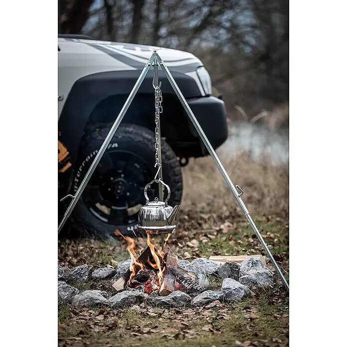 Petromax Dreibeinständer - Grau - Silbernes Camping-Dreibein, das einen Metallkessel über einem Lagerfeuer in Outdoor-Umgebung hält.