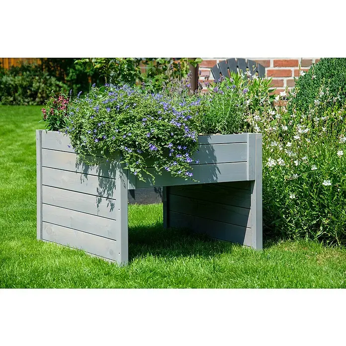 Dobar Mähroboter-GarageL x B x H: 73 x 79 x 56 cm, Grau - Nahaufnahme eines erhöhten Gartenbeets aus Holz mit blühenden Pflanzen, das auf einem grünen Rasen steht und eine stilvolle Gartengestaltung zeigt.