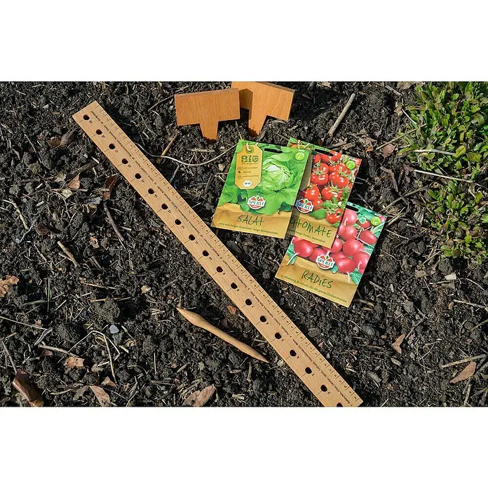 Dobar Starter-Set Anzucht - 1x Pflanzlineal, 1x Pikierstab, 5x Pflanzschild, 3x Samenmischung (Tomaten, Kopfsalat, Radieschen), Beiblatt - Eine Nahaufnahme von Salat-, Tomaten- und Radieschensamen, einem Holzlineal und Markierungsschildern im Garten.