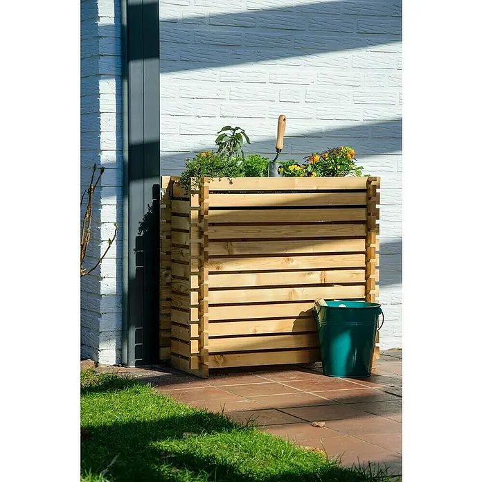 Dobar Hochbeet Stecksystem Larix - L x B x H: 79 x 39 x 79 cm, Holz, Natur - Ein hölzerner Hochbeet-Pflanzkasten mit bunten Blumen und einem kleinen Spaten, daneben ein grüner Eimer, steht vor einer weißen Backsteinmauer.