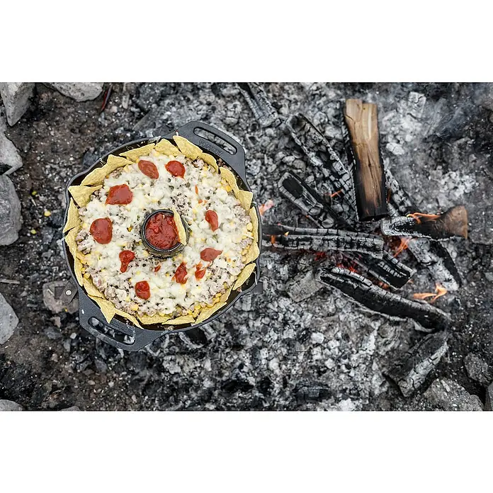 Petromax Geflügelbräter - Gusseisen, Durchmesser: 25 cm - 30 cm - Ein köstlicher Auflauf mit Käse und Tortilla-Chips wird in einer gusseisernen Pfanne über einem Lagerfeuer zubereitet.