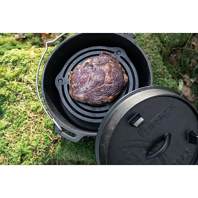 Petromax Grillrost mit Füßen - Gusseisen, Ø x H: 23 x 4,8 cm, Schwarz - Schwarzer gusseiserner Petromax Dutch Oven mit Steak auf einem Grillrost, Deckel angelehnt, bereit zum Outdoor-Kochen.