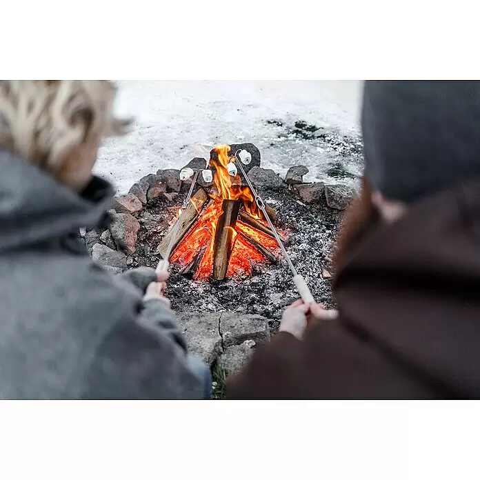 Petromax Grillspieß - Länge: 91 cm, Edelstahl/Buchenholz, Form: Gebogen, 2 Stk. - Zwei Personen rösten Marshmallows an Stöcken über einem knisternden Lagerfeuer in einer schneebedeckten Umgebung.