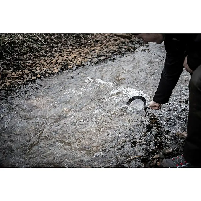 Petromax Grillpfanne - Durchmesser: 14 cm - 20 cm, Höhe: 12 cm, Eisen - Aufnahme einer Person, die mit einer Schaufel Wasser aus einem Bach schöpft, wahrscheinlich im Rahmen einer Umweltstudie oder -überwachung.