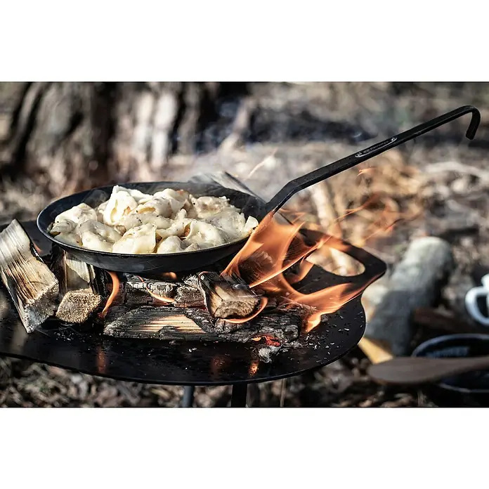 Petromax Grillpfanne - Durchmesser: 14 cm - 20 cm, Höhe: 12 cm, Eisen - Eine Bratpfanne mit Teigtaschen steht über einem offenen Feuer, das auf einer runden Metallbasis entfacht wurde. Outdoor-Kochgeschirr im Einsatz.