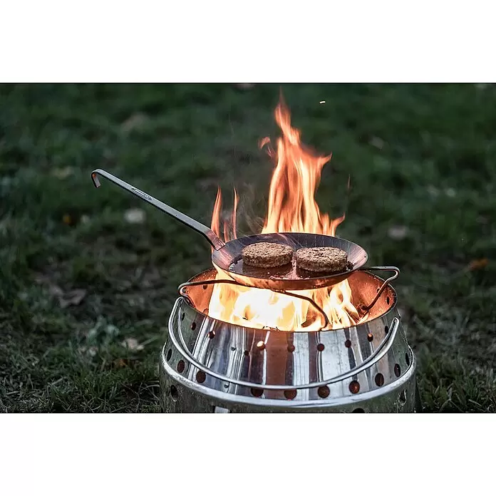 Petromax Grillpfanne - Durchmesser: 17,8 cm - 24 cm, Höhe: 12,6 cm, Eisen - Dunkle Metallpfanne mit zwei Patties brät über glänzender, tragbarer Metall-Feuerstelle mit Flammen.