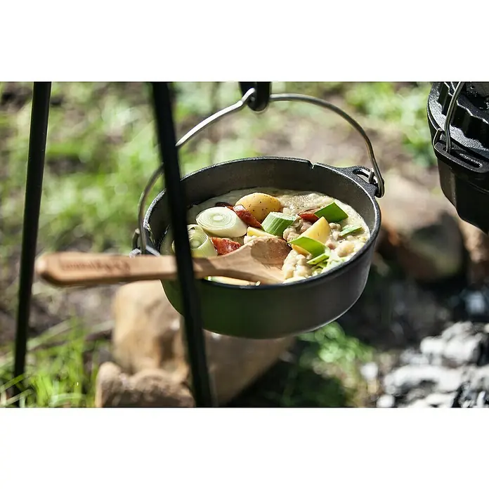 Petromax Dutch Oven - Ø x H: 25,2 x 12 cm, Gusseisen, 1,6 l, Planer Boden - Ein rustikaler Schmortopf hängt über einem Lagerfeuer, gefüllt mit herzhafter Eintopf. Perfekt für Outdoor-Abenteuer und köstliche Mahlzeiten in der Natur.