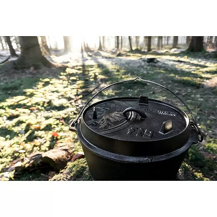 Petromax Dutch Oven - Ø x H: 36,4 x 19,2 cm, Gusseisen, 7,5 l, Planer Boden - Schwarzer gusseiserner Dutch Oven mit Deckel, draußen in einem sonnendurchfluteten Wald.