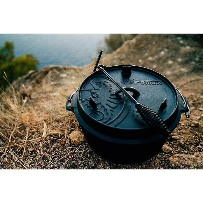 Petromax Dutch Oven - Ø x H: 36,4 x 19,2 cm, Gusseisen, 7,5 l, Planer Boden - Ein Petromax Dutch Oven mit Deckelheber steht auf einem steinigen Untergrund im Freien. Ideal zum Kochen im Freien.