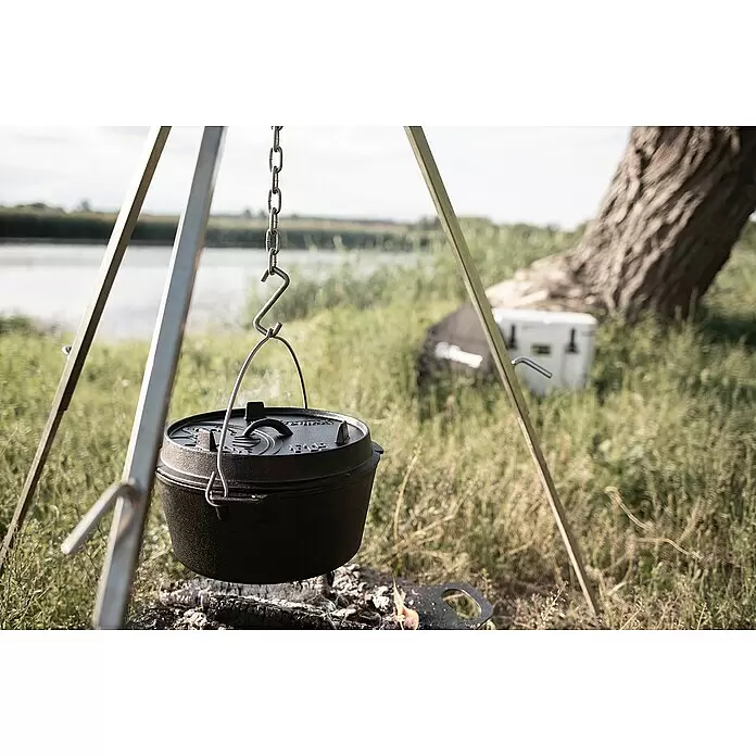 Petromax Dutch Oven - Ø x H: 36,4 x 19,2 cm, Gusseisen, 7,5 l, Planer Boden - Schwarzer Gusseisen-Dutch-Oven dampft über einem Lagerfeuer, hängt an einem Metallstativ im Freien am Fluss.