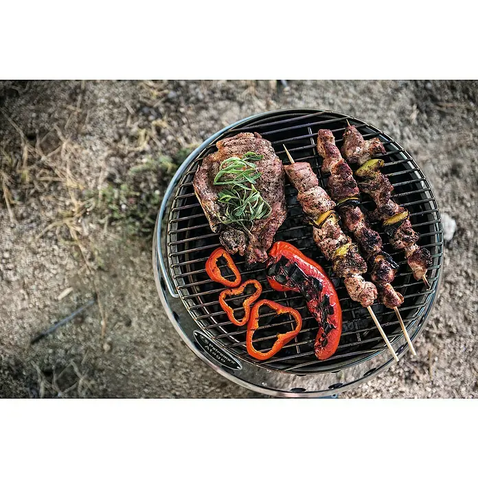 Petromax Holzkohlegrill Atago - Grillfläche (B x T): 45,1 x 44,5 cm, Durchmesser Grillfläche: 34 cm, Silber - Nahaufnahme von einem Petromax Atago Grill mit einem Steak, Paprika und Fleischspießen, alles köstlich zubereitet.