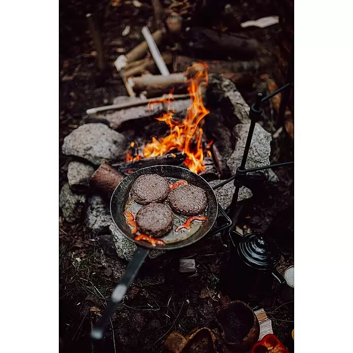 Petromax Grillpfanne - Durchmesser: 24,5 cm - 32 cm, Höhe: 17 cm, Eisen - Drei Burgerpatties und rote Paprika in einer Pfanne über einem knisternden Lagerfeuer, daneben ein schwarzer Kessel.