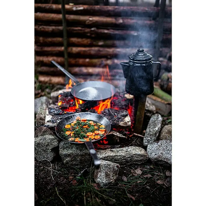 Petromax Grillpfanne - Durchmesser: 24,5 cm - 32 cm, Höhe: 17 cm, Eisen - Zubereitung eines Outdoor-Menüs am Lagerfeuer mit Pfannengerichten und einer Kaffeekanne.