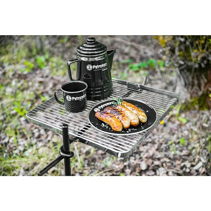 Petromax Perkolator Perkomax - Schwarz, 1,3 l - Outdoor-Szene mit Petromax-Kaffeekanne, Tasse und Wurst auf einem Grill, ideal für Campingausflüge in der Natur.
