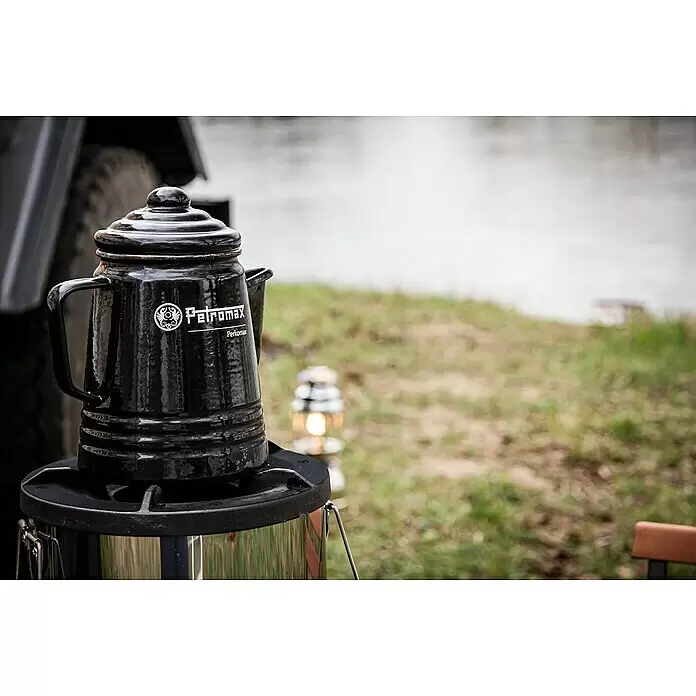 Petromax Perkolator Perkomax - Schwarz, 1,3 l - Schwarzer Petromax Perkomax Kaffeebereiter auf Campingkocher im Freien, mit verschwommenem See und Laterne.