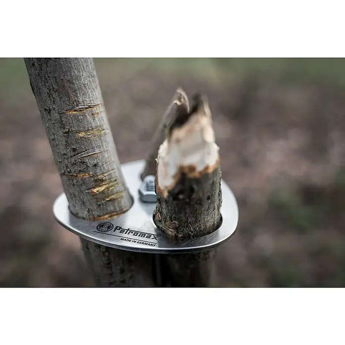 Petromax Dreibein-Ring - Durchmesser: 10,5 cm, Edelstahl - Nahaufnahme eines Petromax Bushcraft-Kochers mit zwei Ästen, die durch eine Metallplatte befestigt sind. Hergestellt in Deutschland für Outdoor-Abenteuer.