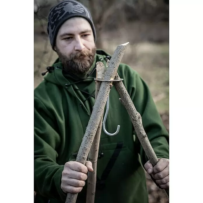 Petromax Dreibein-Ring - Durchmesser: 10,5 cm, Edelstahl - Person hält zwei Holzstöcke, verbunden durch Metallring und S-Haken, als robustes Outdoor-Aufhängesystem.
