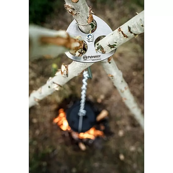 Petromax Dreibein-Ring - Durchmesser: 10,5 cm, Edelstahl - Silberner Petromax Stativadapter, der drei Äste über einem Lagerfeuer hält, mit einem schwarzen Topf an einer Kette.