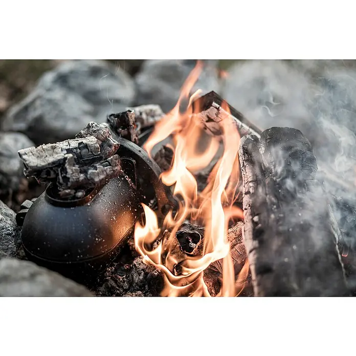 Petromax Kartoffelbräter - L x B x H: 29,1 x 17 x 15,4 cm, Gusseisen - Schwarzer Topf auf einem Lagerfeuer. Ein rustikales Kochutensil inmitten von Flammen und Holz, ideal für Outdoor-Abenteuer und rustikale Mahlzeiten.