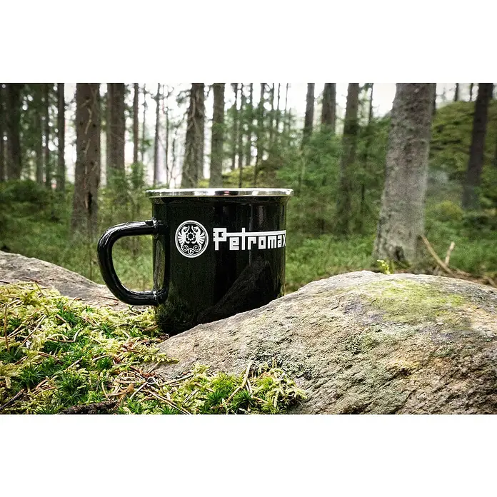 Petromax Tasse - 370 ml, Schwarz - Petromax Emaille Tasse in Schwarz, perfekt für Outdoor-Abenteuer. Robuste Tasse mit Petromax Logo vor einem Waldhintergrund.